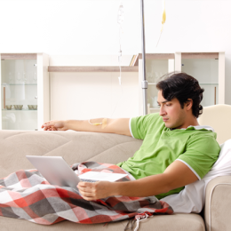 Man sitting on the couch using his laptop while he is connected to home infusion