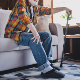 Man sitting on couch holding knee and his cane