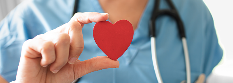 Medical professional with stethoscope holding up a red heart