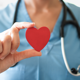 Medical professional with stethoscope holding up a red heart