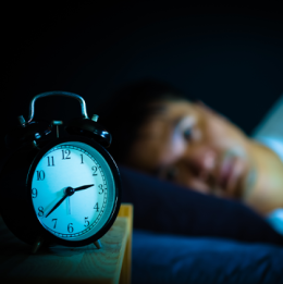 Close up of clock with man lying in bed with eyes open in blurred background